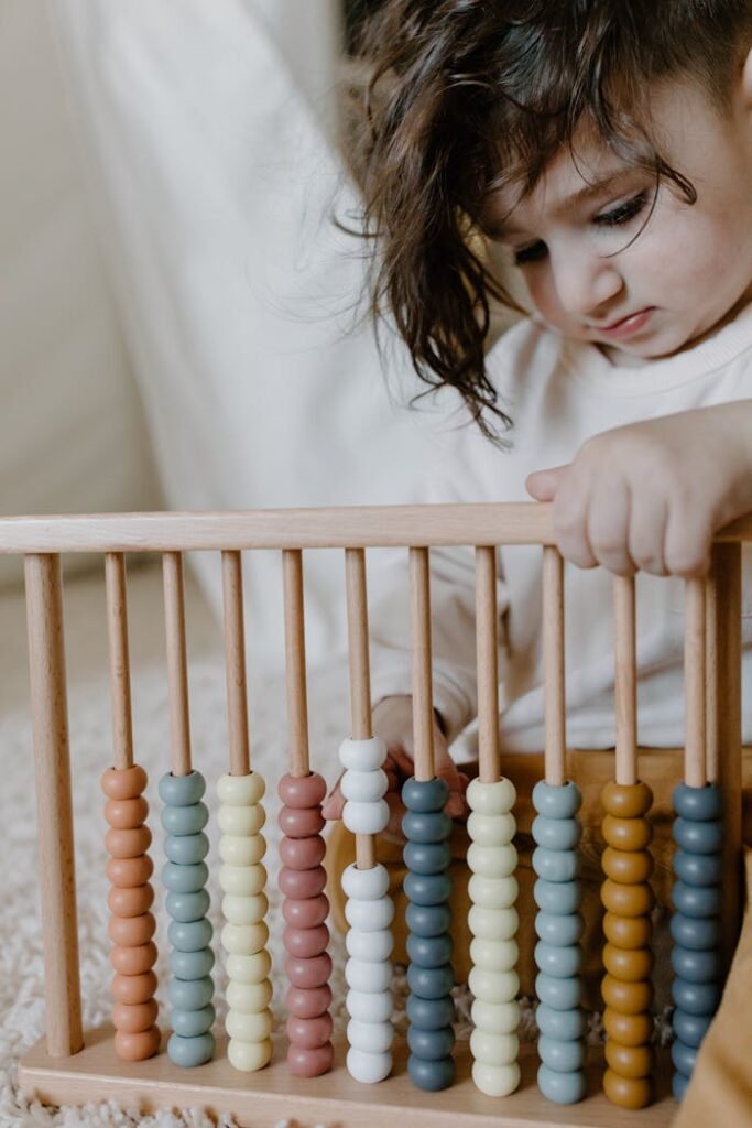 Cute child with curly hair explores a wooden abacus indoors, learning numbers and colors.