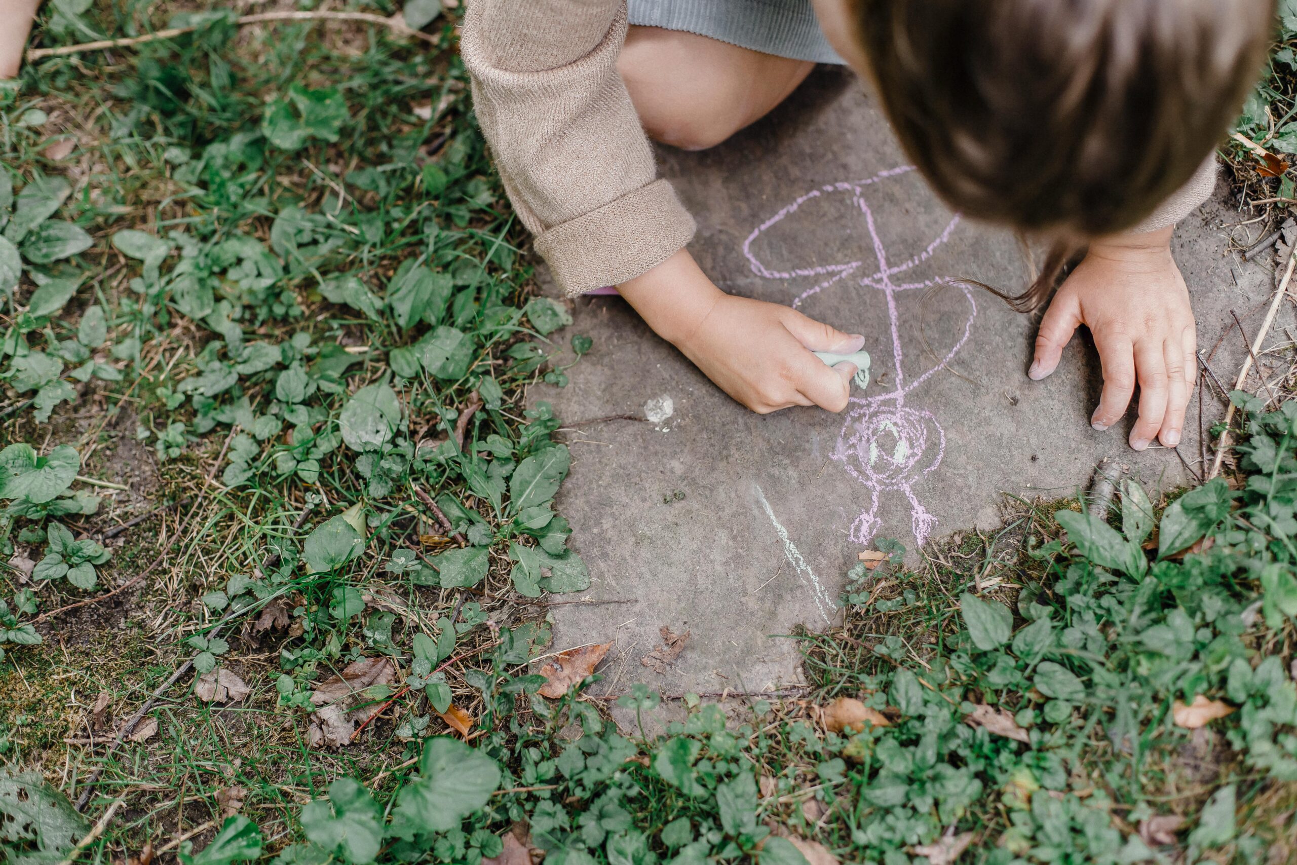 Young child enjoying outdoor creativity drawing with chalk on pavement.